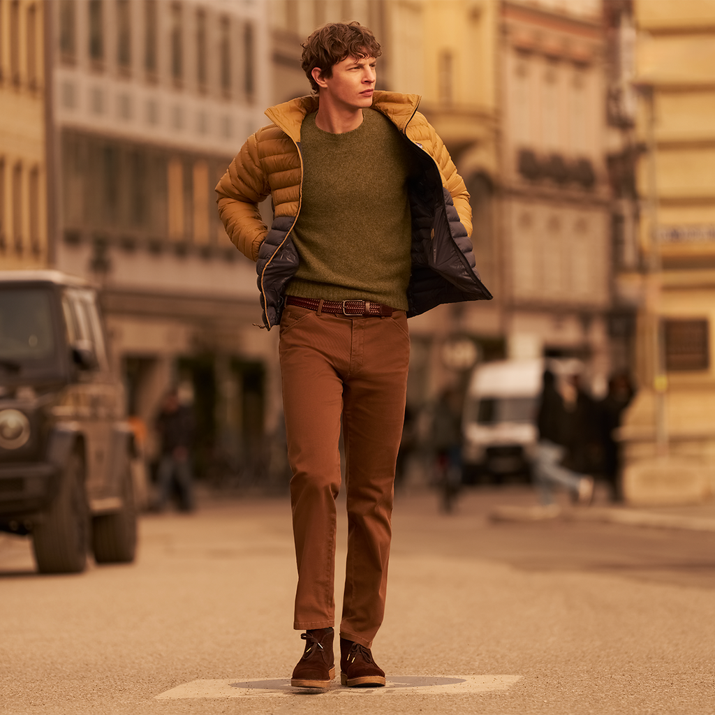 Man in a green sweater and brown pants standing on a street with buildings in the background